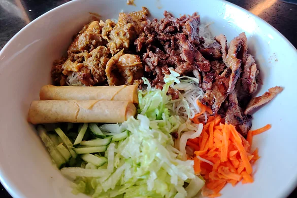 Vermicelli bowl with grilled meats, spring rolls, lettuce, cucumber and pickled carrot